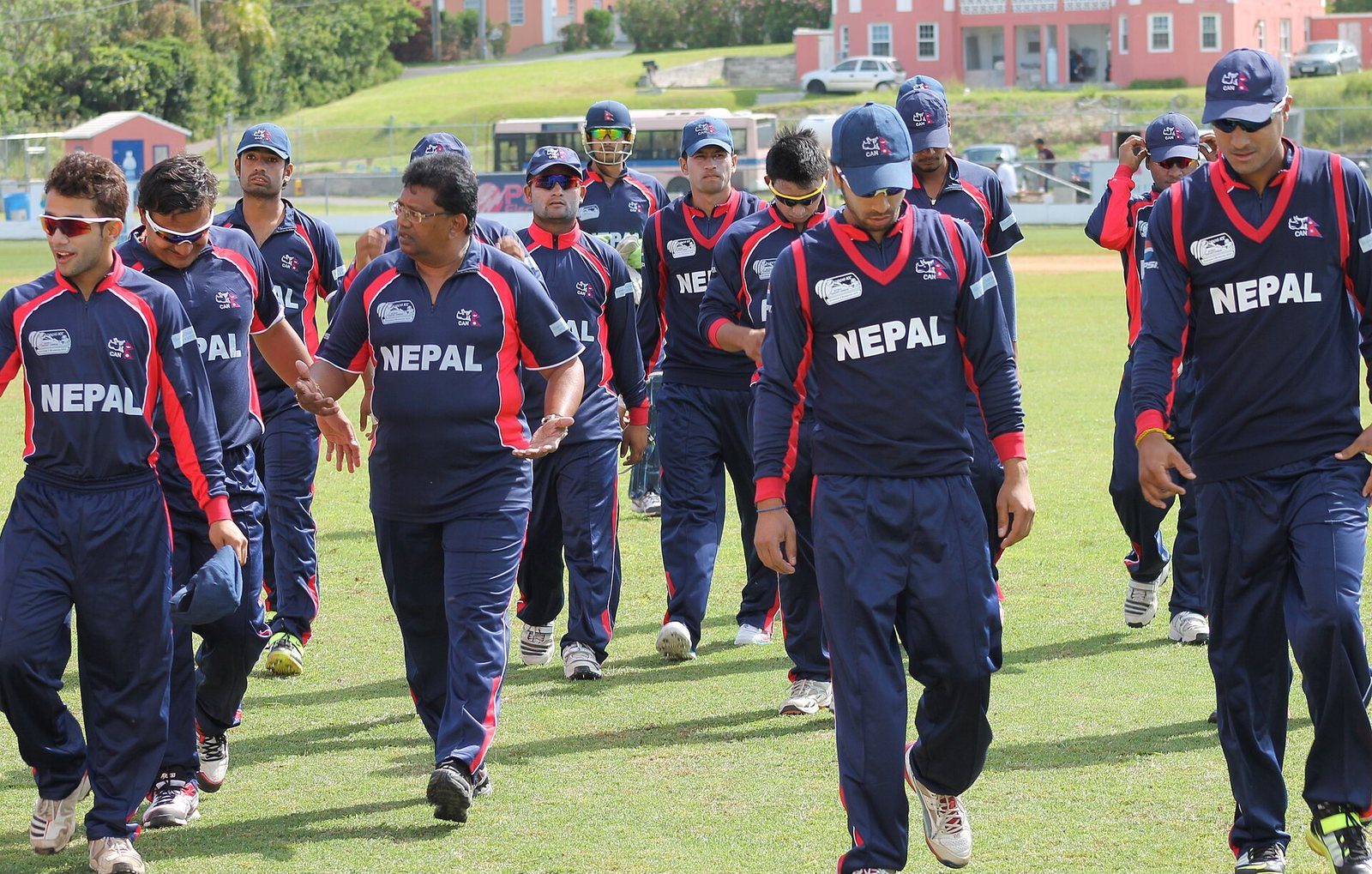 Members of the Nepal national cricket team in navy blue Nepal kit walking together on a grass field.