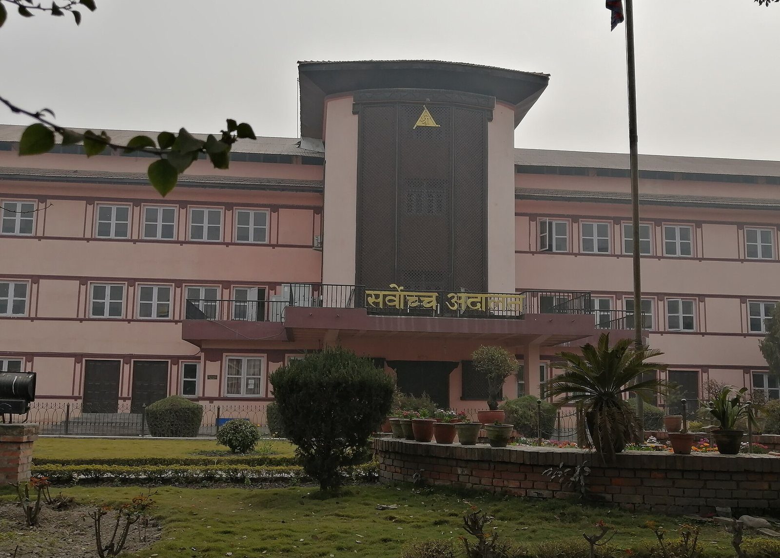 The Supreme Court of Nepal's building in Kathmandu, with its distinctive tower and pink facade, seen from the garden in front.