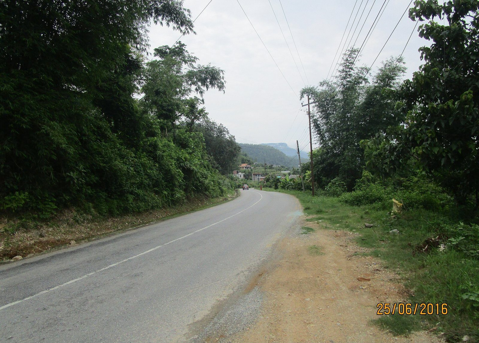 The Prithvi Highway winding through green hillsides in Nepal, with power lines overhead and hills in the distance.