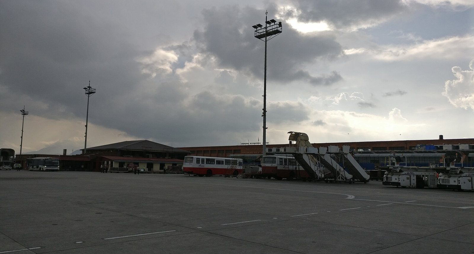 An evening view of Tribhuvan International Airport's terminal building in Kathmandu, seen from the boarding area under a cloudy sky.