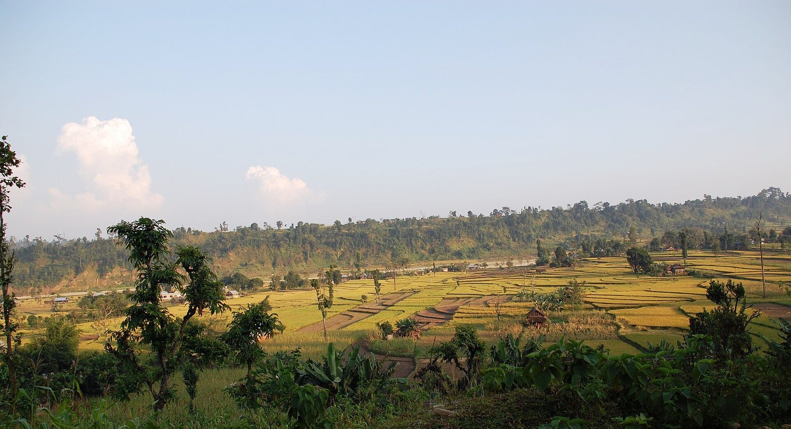 A landscape view of green rice terraces and village houses in Kavrepalanchok District, Nepal, under a clear sky.
