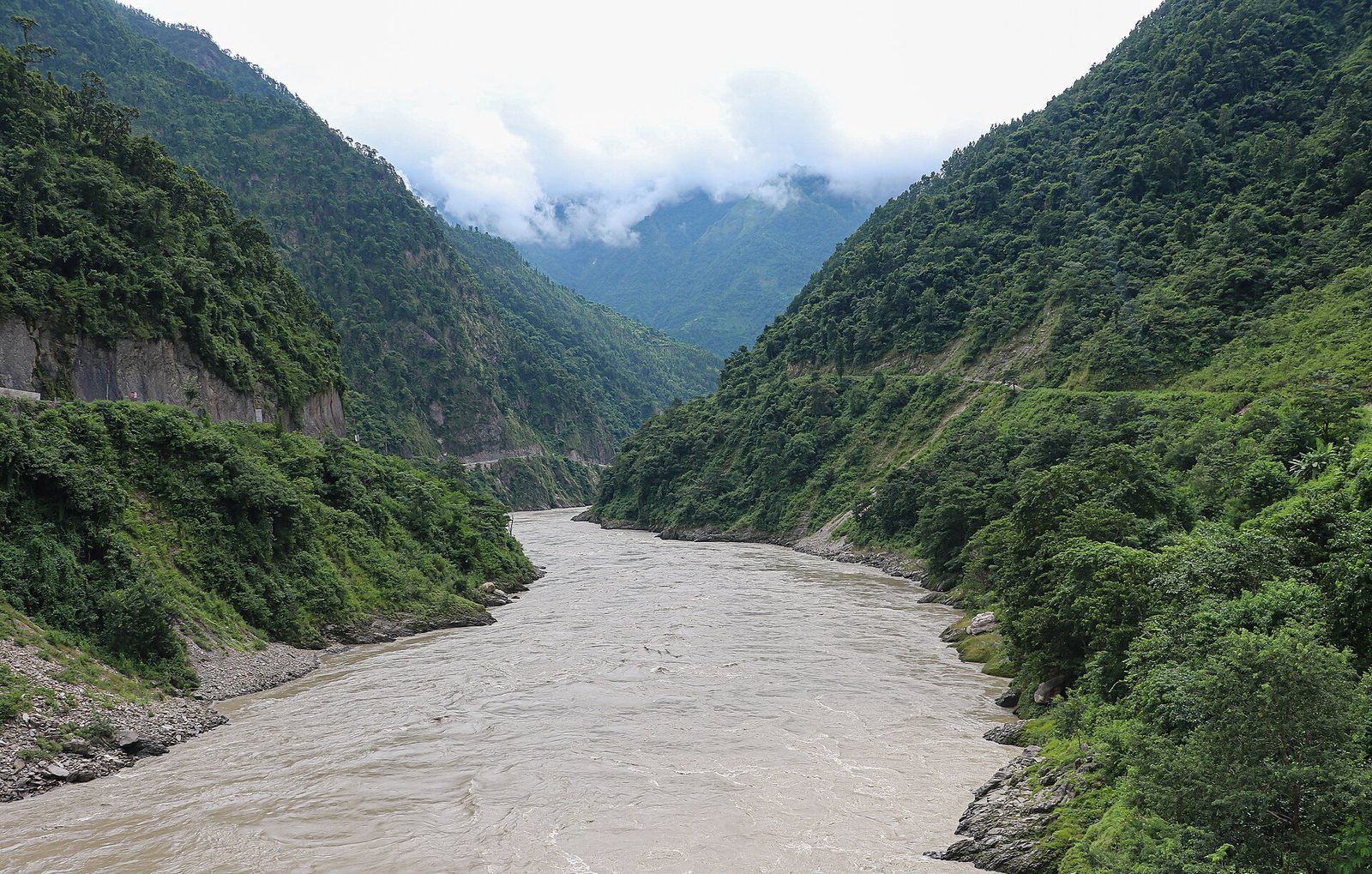 The wide, fast-flowing Trishuli River seen from the old bridge at Mugling, framed by green forested hills.