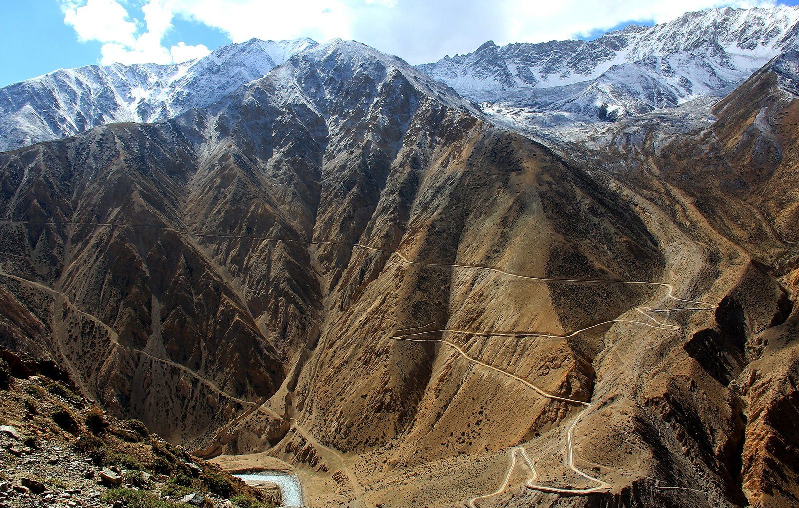 A winding mountain road snakes down a steep, barren Himalayan slope toward the Hilsa border crossing in Humla District, Nepal.
