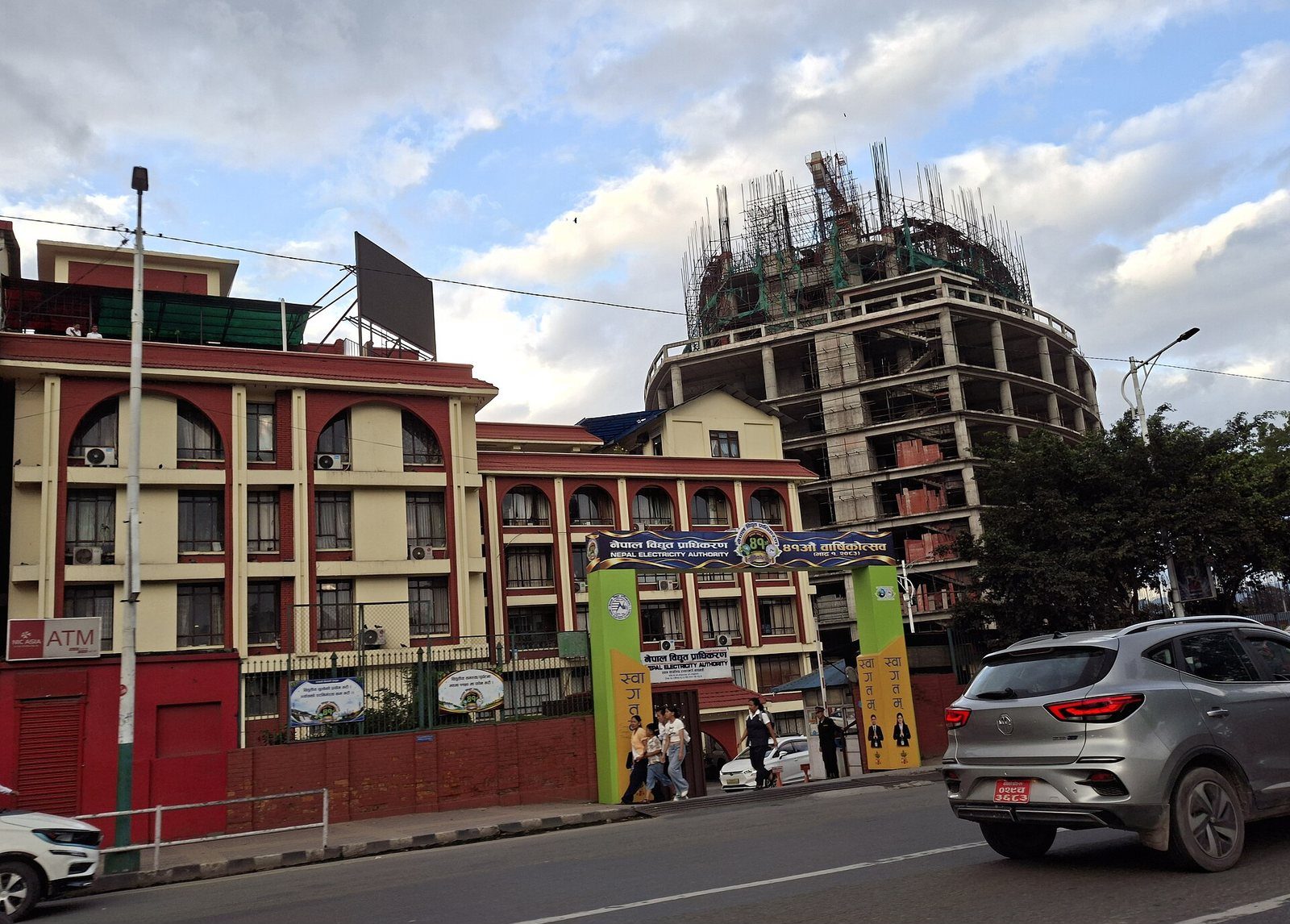 The Nepal Electricity Authority's head office building in Kathmandu, a multi-story structure with a gated entrance and a partially constructed tower rising behind it.