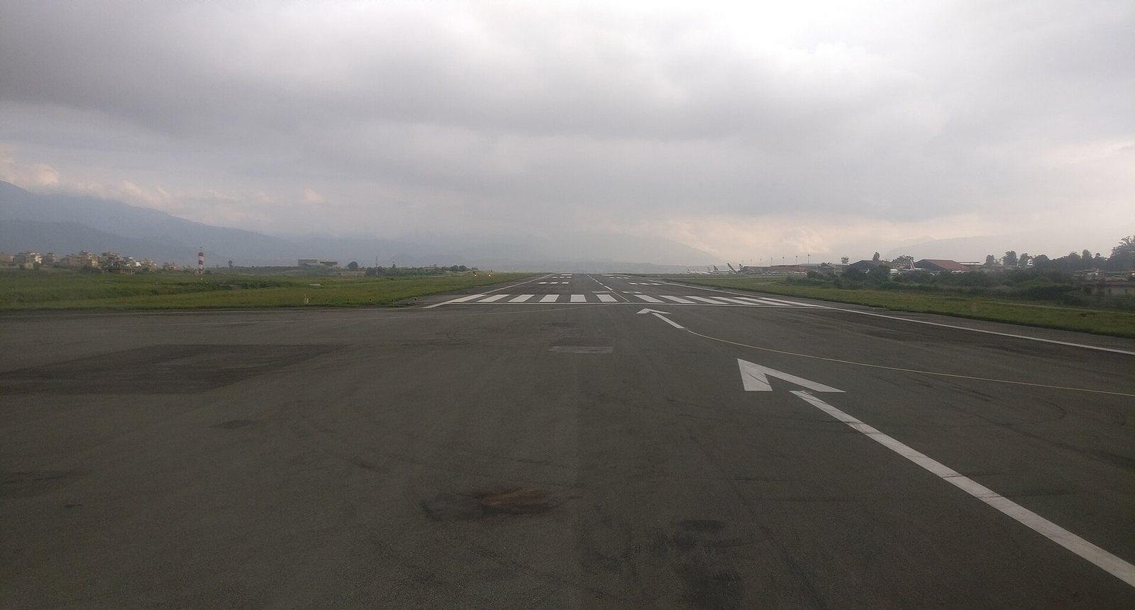 A view of the runway at Tribhuvan International Airport under an overcast sky, seen from a departing aircraft.