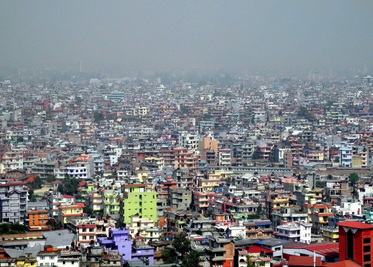 An aerial view of densely packed buildings across the Kathmandu valley under a hazy sky.